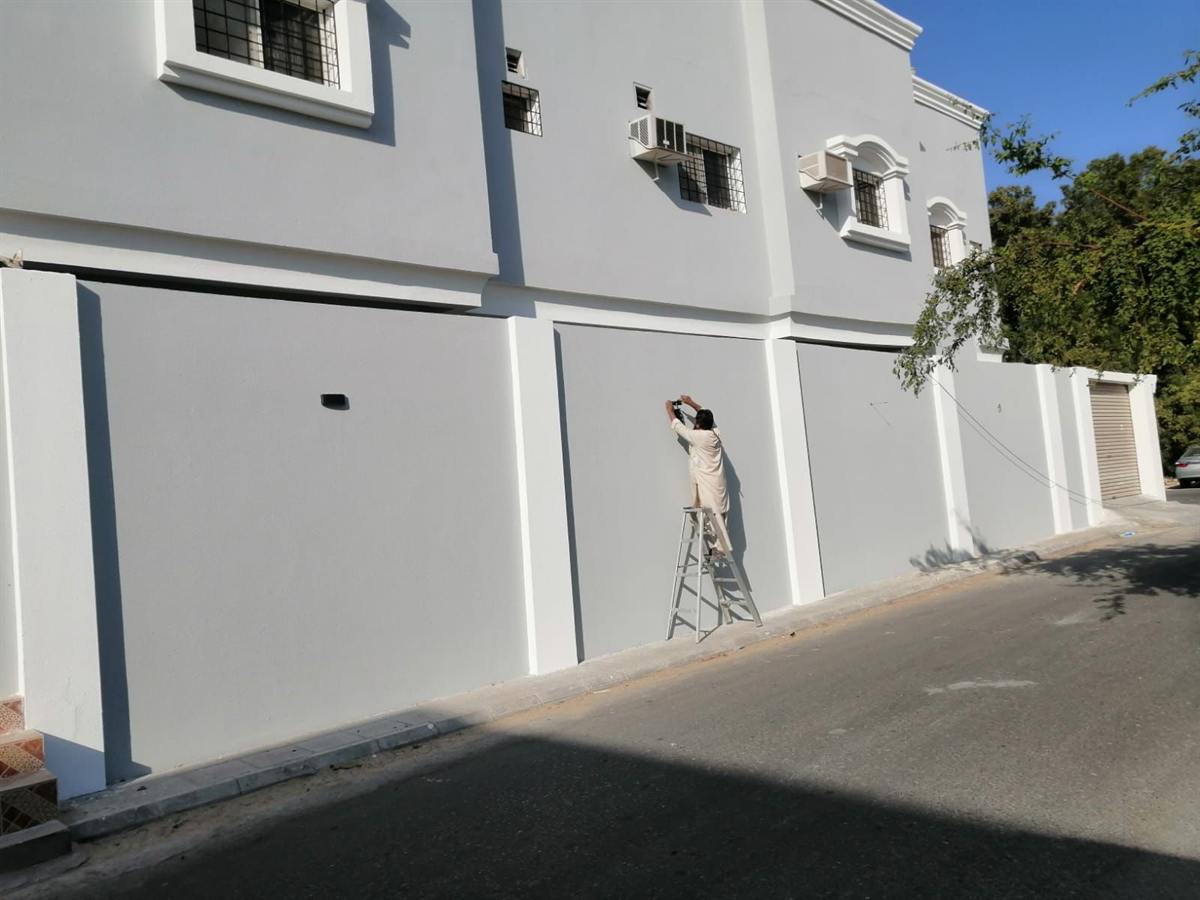 عامل ينفذ أصباغ خارجية على سور مبنى